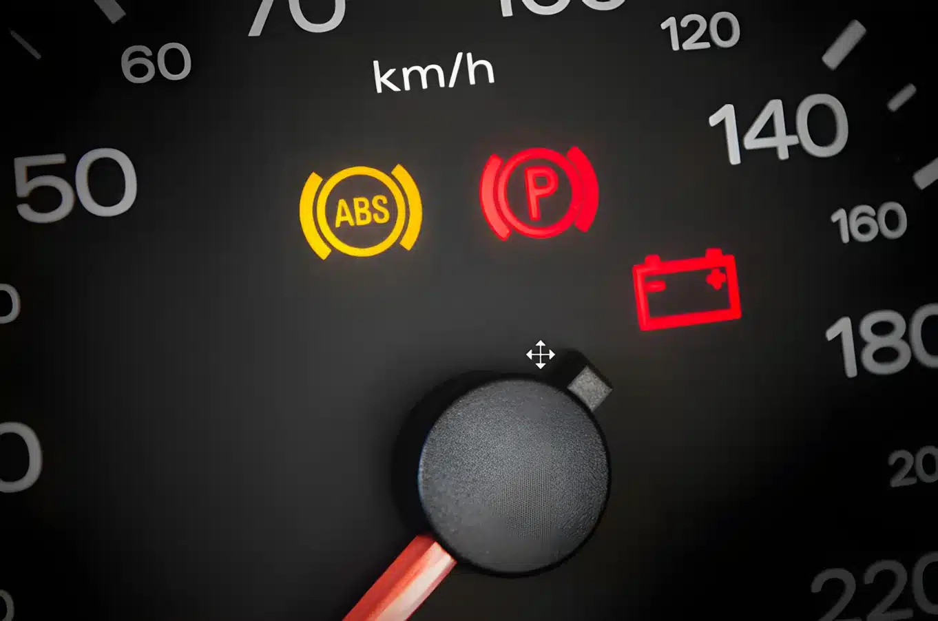 Close-up of a car speedometer with illuminated warning lights for ABS, parking brake, and battery, indicating potential issues. The needle points near zero km/h.