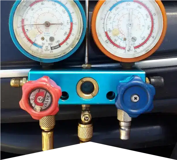 Auto Air Conditioning & Heater Repair in Clive, IA At Westside Auto Pros. A close-up of a blue HVAC manifold gauge set with two dials, red and blue control knobs, and attached brass hoses, used for measuring pressure in air conditioning systems.