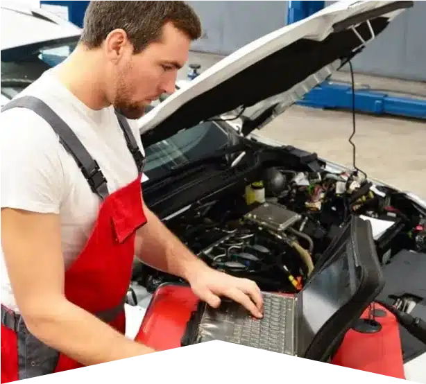 Auto Diagnostics in Clive, IA At Westside Auto Pros. A male mechanic in red overalls uses a diagnostic laptop computer next to a car with its hood open inside an automotive repair shop.
