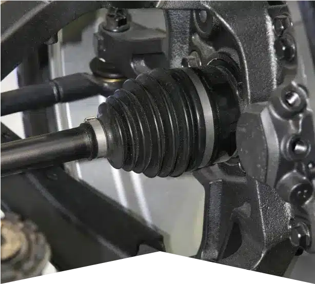 Axle Repair & Services in Clive, IA At Westside Auto Pros. Close-up view of a car’s CV (constant velocity) joint and driveshaft, showing the rubber boot, metal components, and part of the suspension system in a mechanical setting.