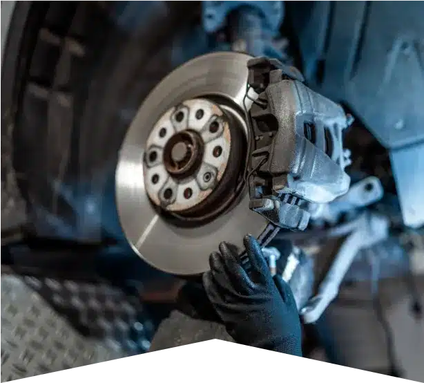 Brake Repair in Clive, IA At Westside Auto Pros. A close-up of a mechanic’s gloved hands working on a car’s disc brake system, focusing on the metal brake rotor and caliper inside a vehicle repair shop.