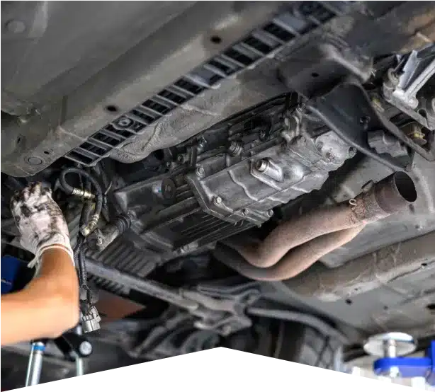 Drivetrain Repair in Clive, IA At Westside Auto Pros. A mechanic’s gloved hands work underneath a raised car, focusing on engine and exhaust components. The underside of the vehicle and various mechanical parts are visible.