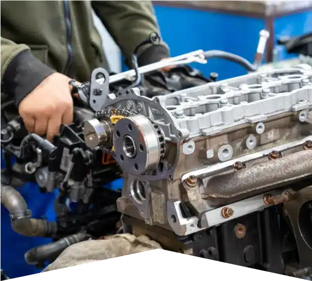 Engine Repair in Clive, IA At Westside Auto Pros. A person in a green jacket works on assembling or repairing a car engine, focusing on the cylinder head and timing mechanism in a workshop setting.