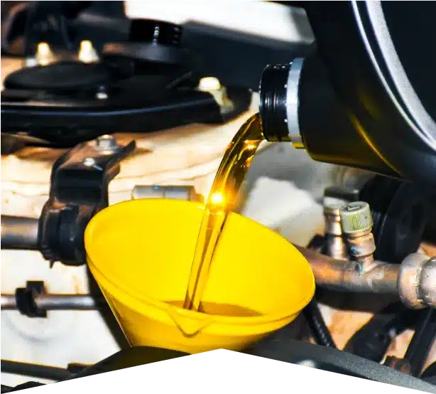 Preventative Maintenance & Oil Change in Clive, IA At Westside Auto Pros. Close-up of motor oil being poured from a bottle into a yellow funnel placed in a car engine during an oil change. The engine components and funnel are clearly visible.