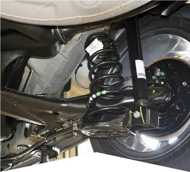 Shocks & Struts Repair in Clive, IA At Westside Auto Pros. Close-up view of a car’s rear suspension system, showing a coil spring, shock absorber, and surrounding mechanical components near a wheel under the vehicle.