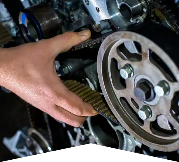 Timing Belt Replacement in Clive, IA At Westside Auto Pros. A persons hand adjusting a timing belt on an exposed car engine, showing various gears and mechanical components.