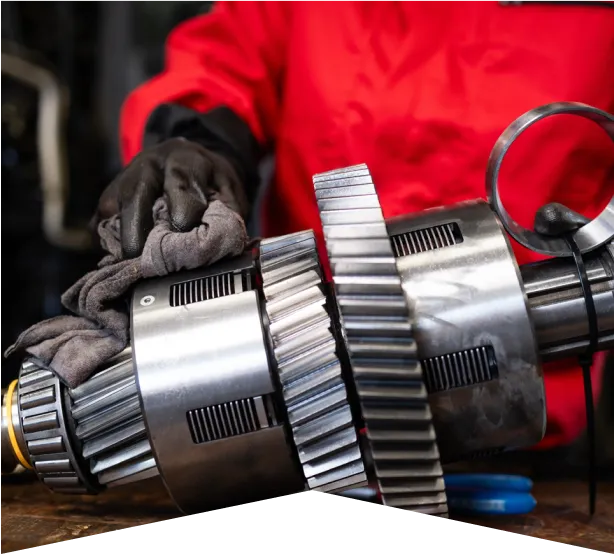 Transmission Repair & Replacement in Clive, IA At Westside Auto Pros. A person wearing black gloves and a red jacket cleans a large metal gear mechanism with a cloth, likely in an industrial or mechanical workshop setting.