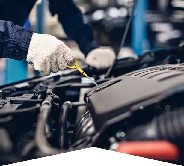 Vehicle Inspection in Clive, IA At Westside Auto Pros. A person wearing white gloves checks a car engine with a dipstick in an auto repair shop. The car hood is open, and the person is dressed in a dark blue uniform.