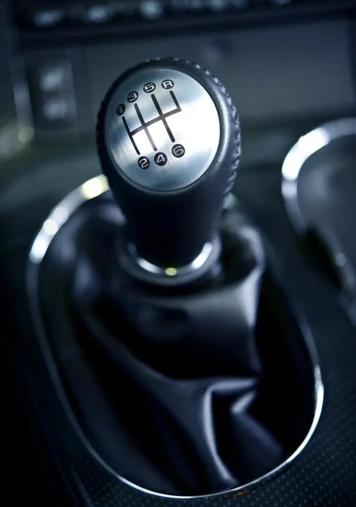 Clutch Repair and Maintenance in Clive, IA At Westside Auto Pros. A close-up of a manual car gear shift knob displaying a 6-speed shift pattern with reverse gear, surrounded by a black leather boot and silver trim.
