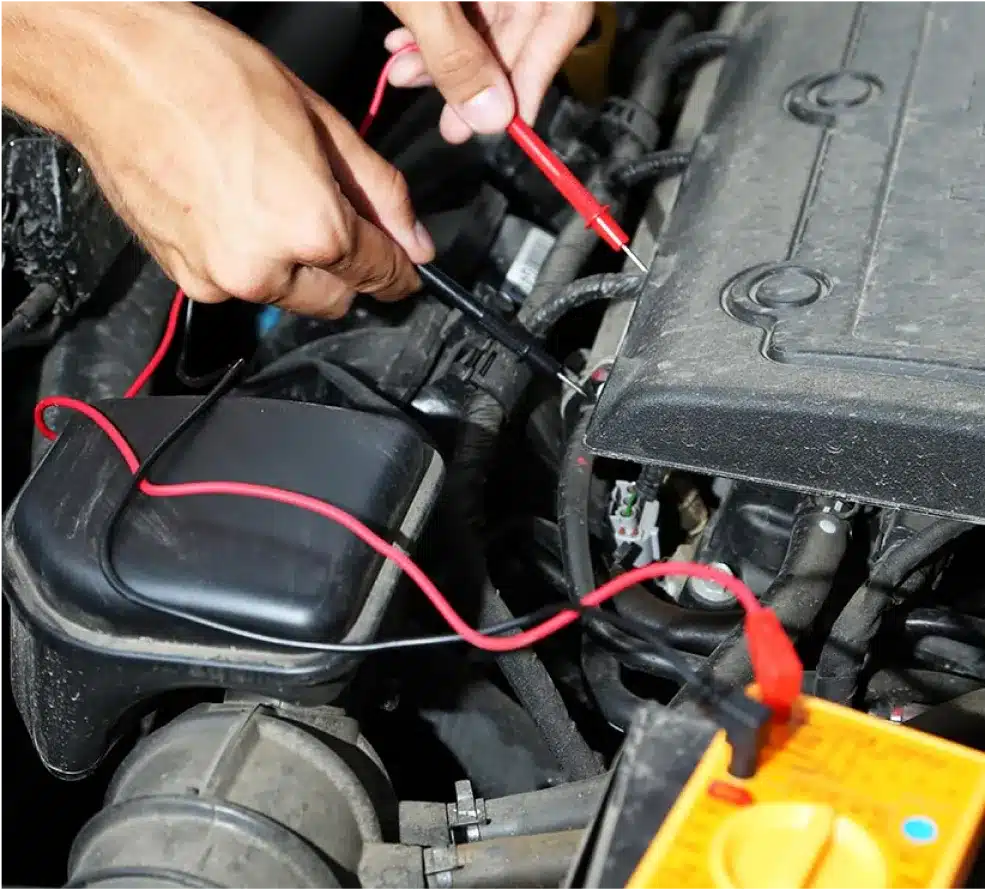ADAS Calibration & Electrical System Repair in Clive, IA At Westside Auto Pros. A person uses a multimeter to check electrical connections under the hood of a car, holding the red and black probes to engine components with visible wires and car parts.