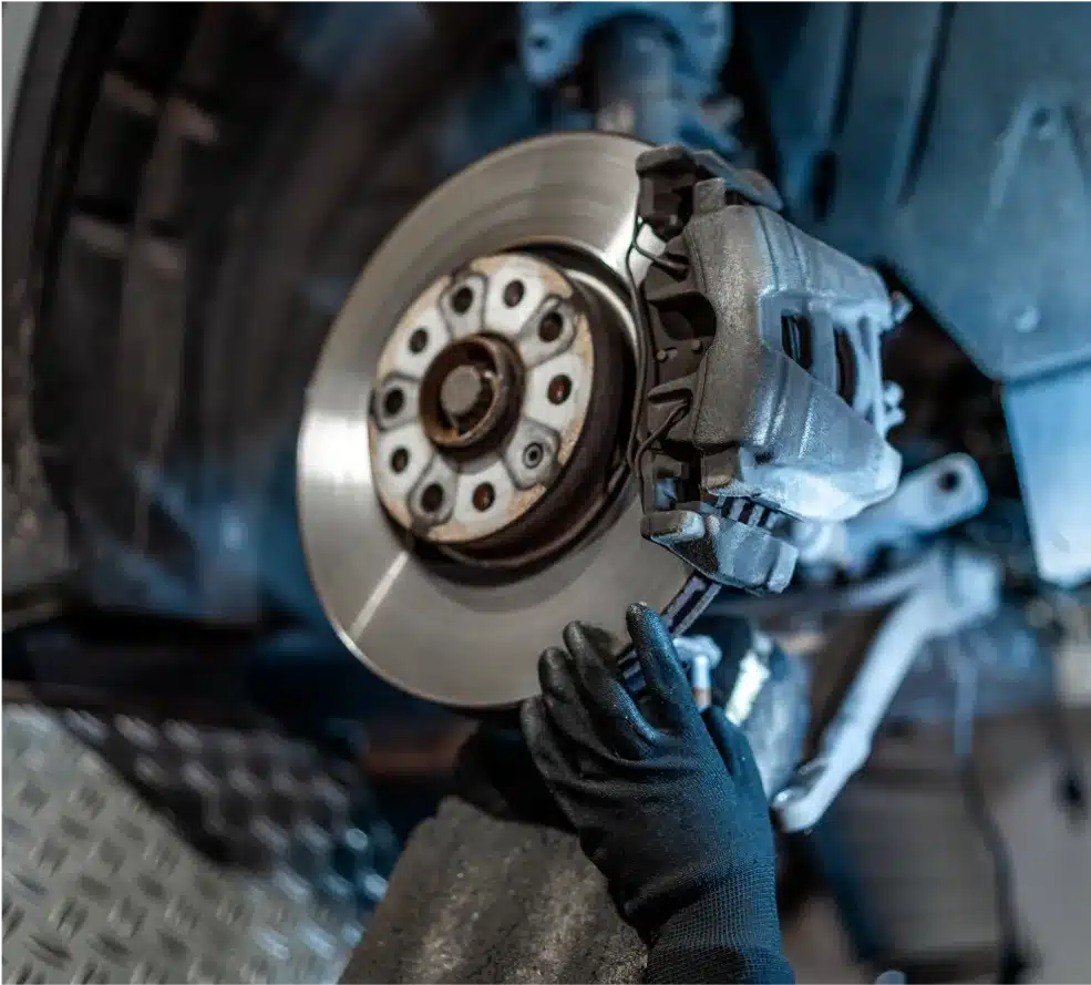 Brake Repair in Clive, IA At Westside Auto Pros. A person wearing black gloves is installing or inspecting a cars brake disc and caliper on a lifted vehicle in an auto repair shop.