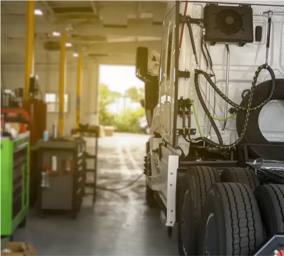 Diesel Repair in Clive, IA At Westside Auto Pros. A white semi-truck is parked inside a well-lit maintenance garage, with tools and equipment visible along the sides and the truck’s rear tires in the foreground.