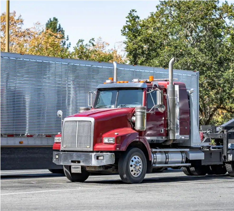 Fleet Maintenance Services in Clive, IA At Westside Auto Pros. A red semi-truck with silver exhaust pipes is parked on a street next to a large, metal-sided trailer, with trees and a blue sky in the background.