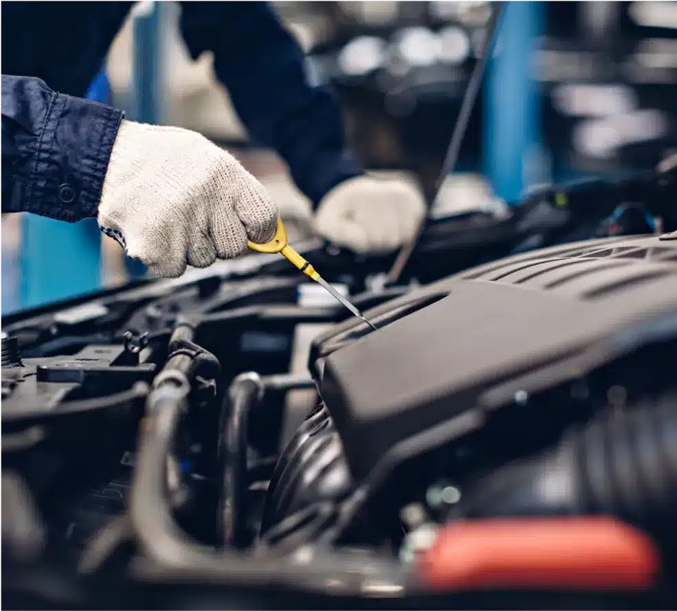Vehicle Inspections in Clive, IA At Westside Auto Pros. A person wearing white gloves checks the oil level of a car engine using a dipstick in a well-lit auto repair shop.