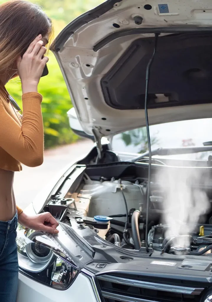 Radiator Repair & Maintenance in Clive, IA At Westside Auto Pros. A woman stands by her car with the hood open, looking at the steaming engine while talking on her phone, possibly seeking assistance for a breakdown.