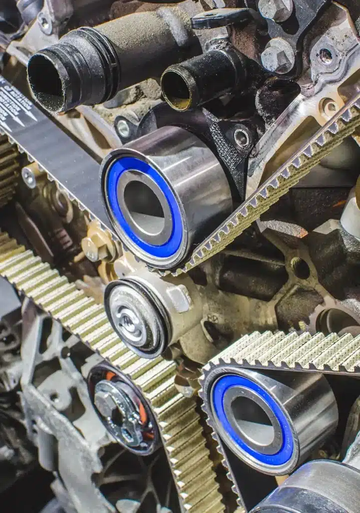 Timing Belt Replacement in Clive, IA At Westside Auto Pros. Close-up view of an automotive engine showing timing belts, pulleys, and metal components, highlighting the mechanical details and texture of the machinery.